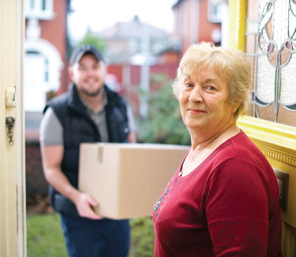 A senior woman holding the door for a mover carrying a box